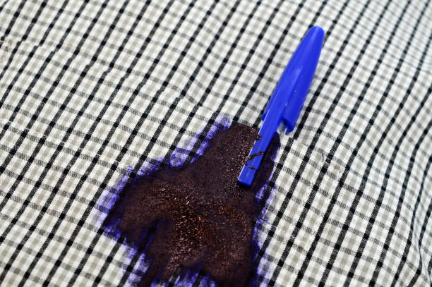 A broken blue pen leaks ink on a plaid fabric, illustrating a common clothing stain problem.